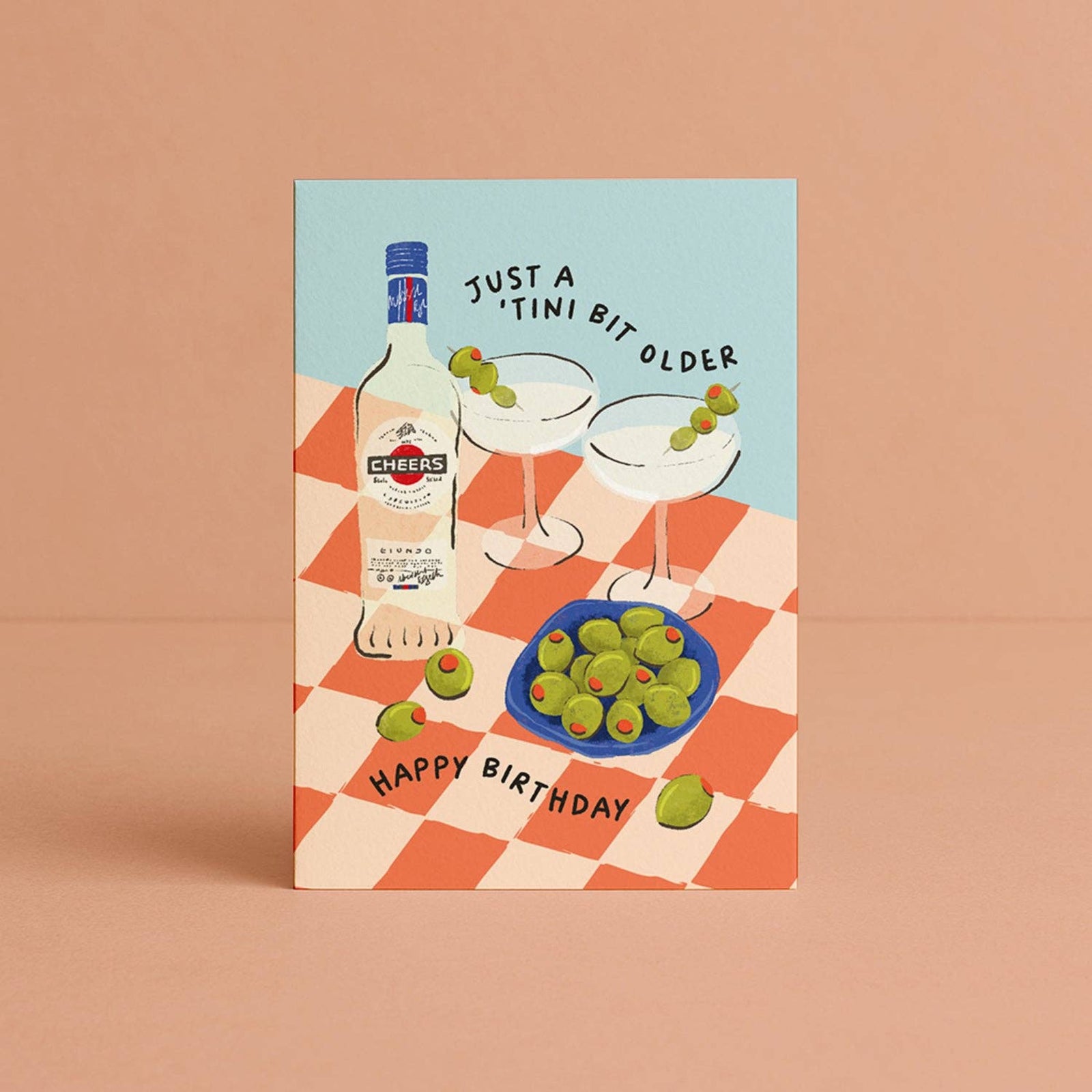 Birthday card with illustration of a bottle, glasses, and olives on a checkered tablecloth.