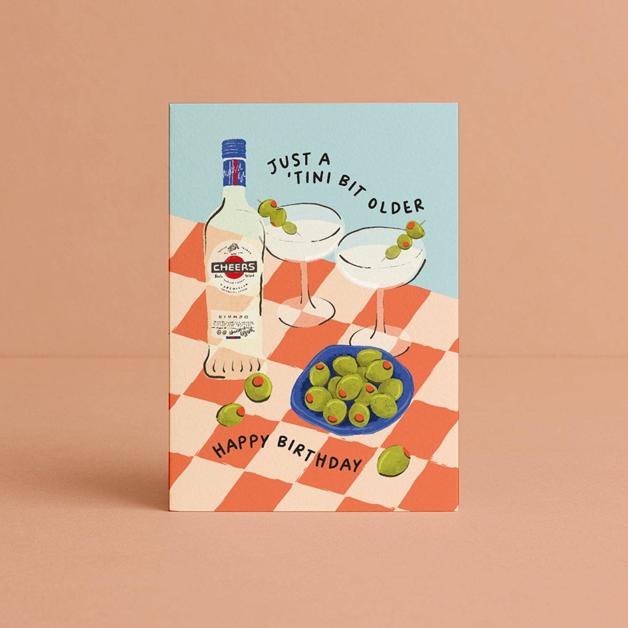 Birthday card with illustration of a bottle, glasses, and olives on a checkered tablecloth.