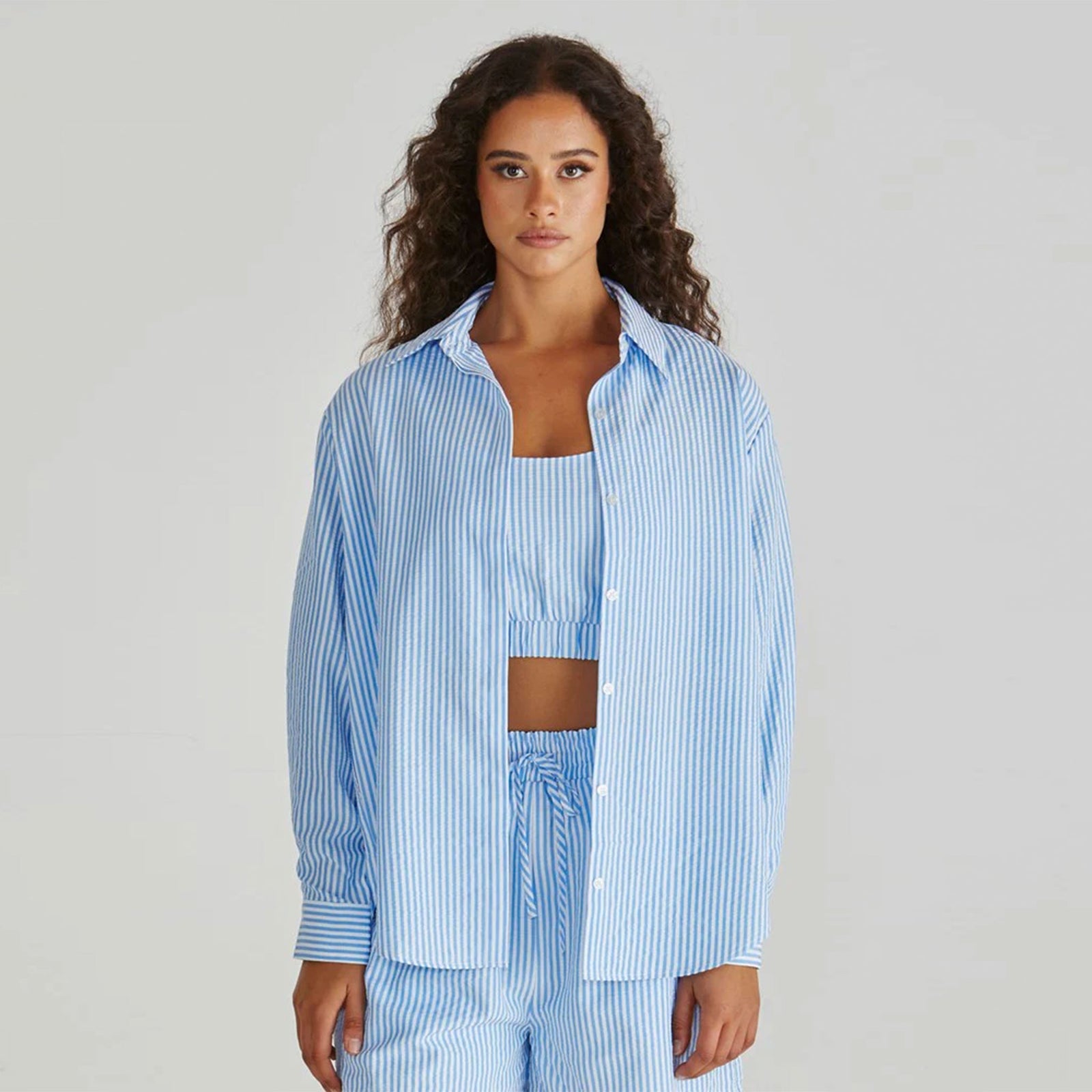 Woman wearing a blue striped shirt and pants on a gray background