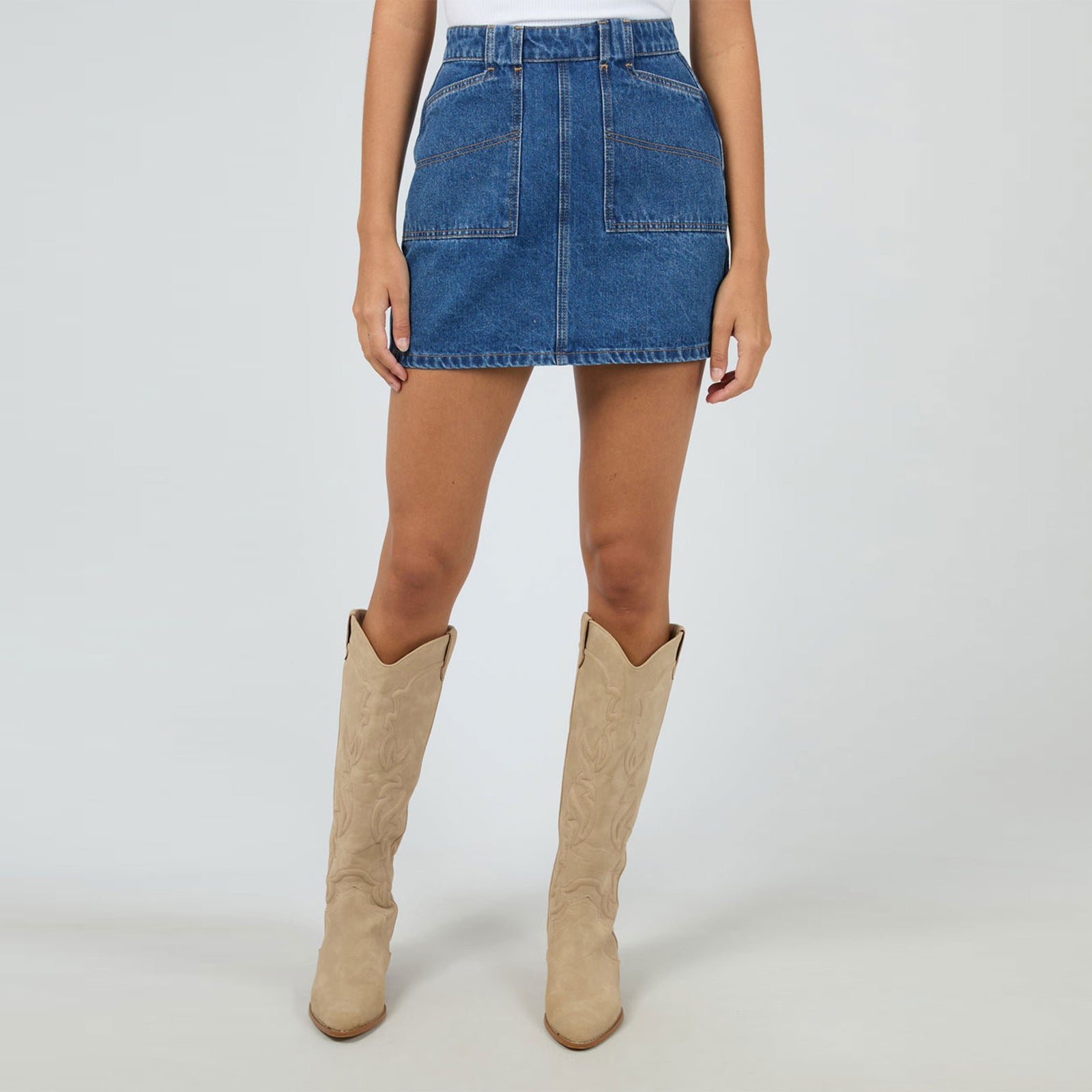 Woman wearing a white t-shirt and blue denim skirt on a plain background