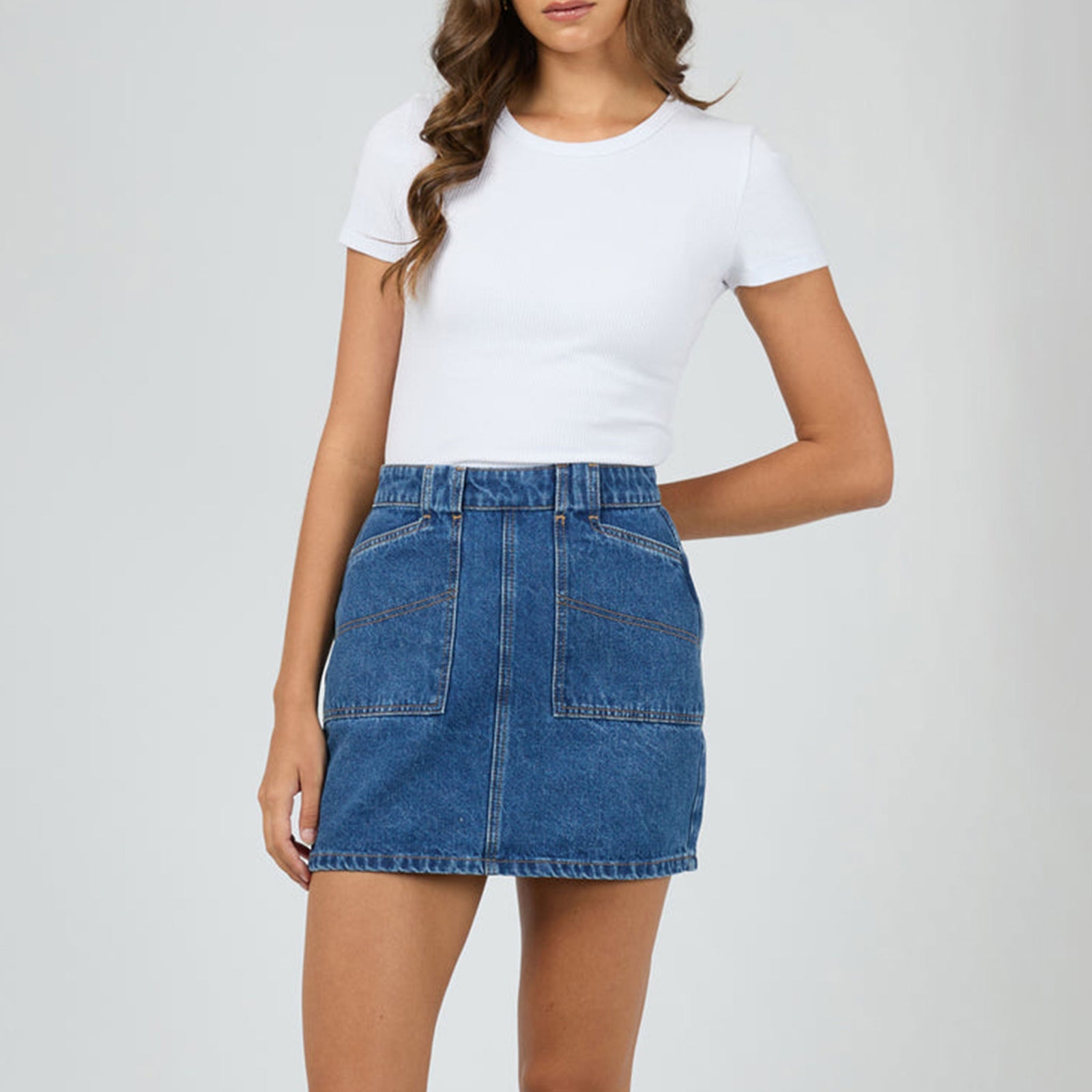 Woman wearing a white t-shirt and blue denim skirt on a plain background