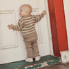 Baby in a brown and white striped outfit standing on a porch.