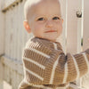Baby wearing a brown and beige striped sweater standing outdoors.