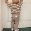 Child wearing a brown and white striped sweater and pants standing against a white door.