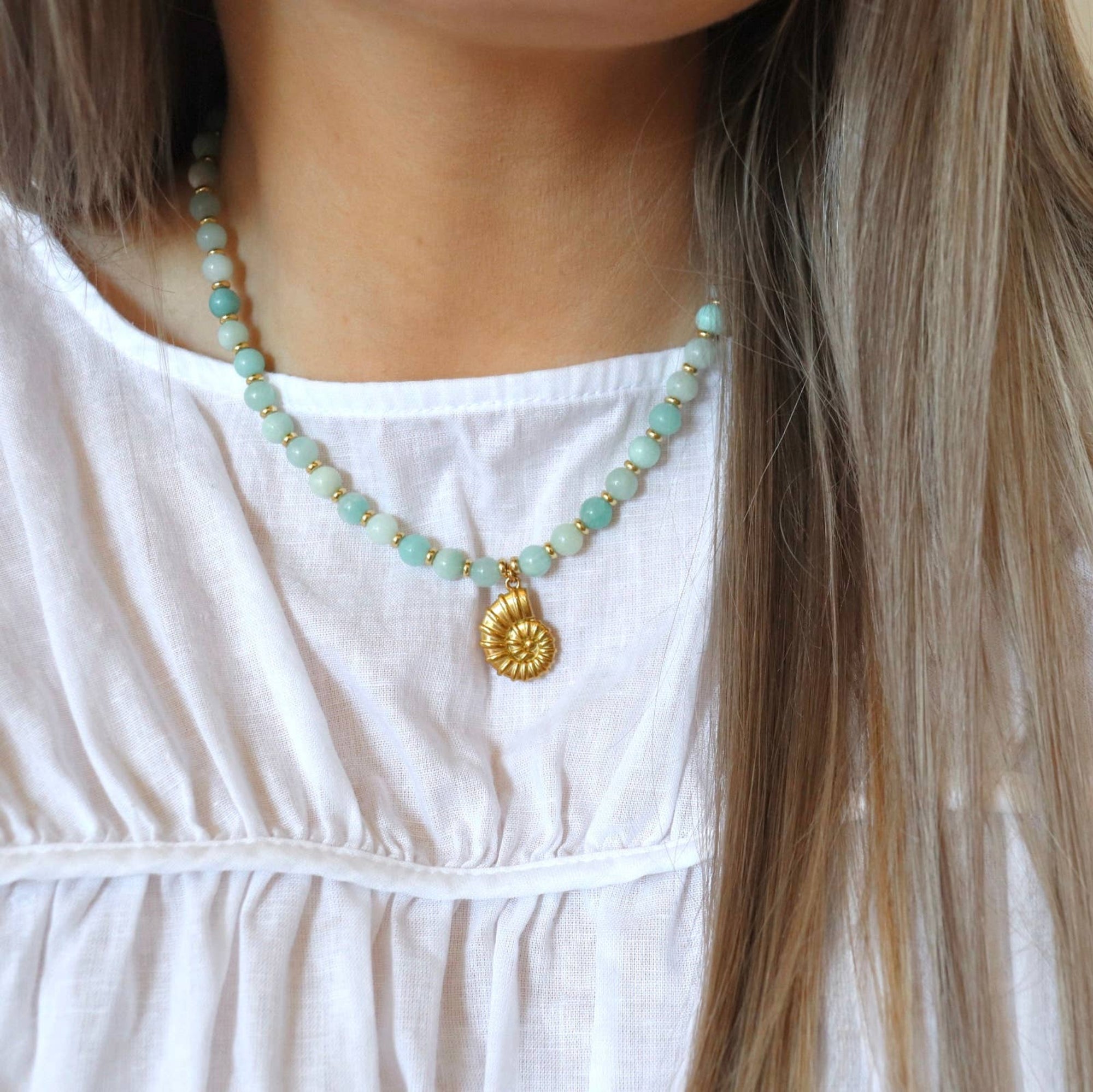Necklace with turquoise beads and a gold pendant worn by a person in a white top.