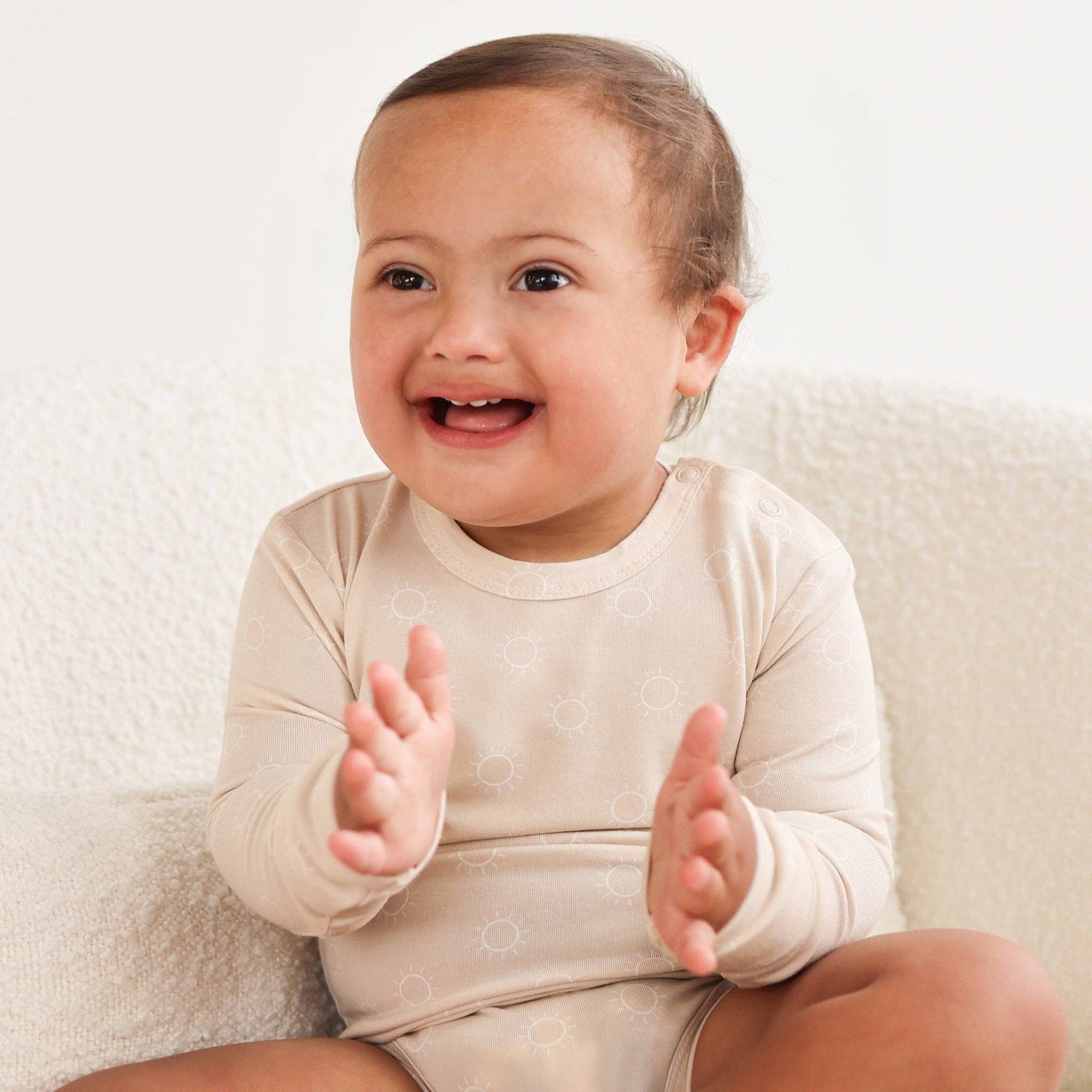 Baby clapping hands wearing a white onesie on a light background
