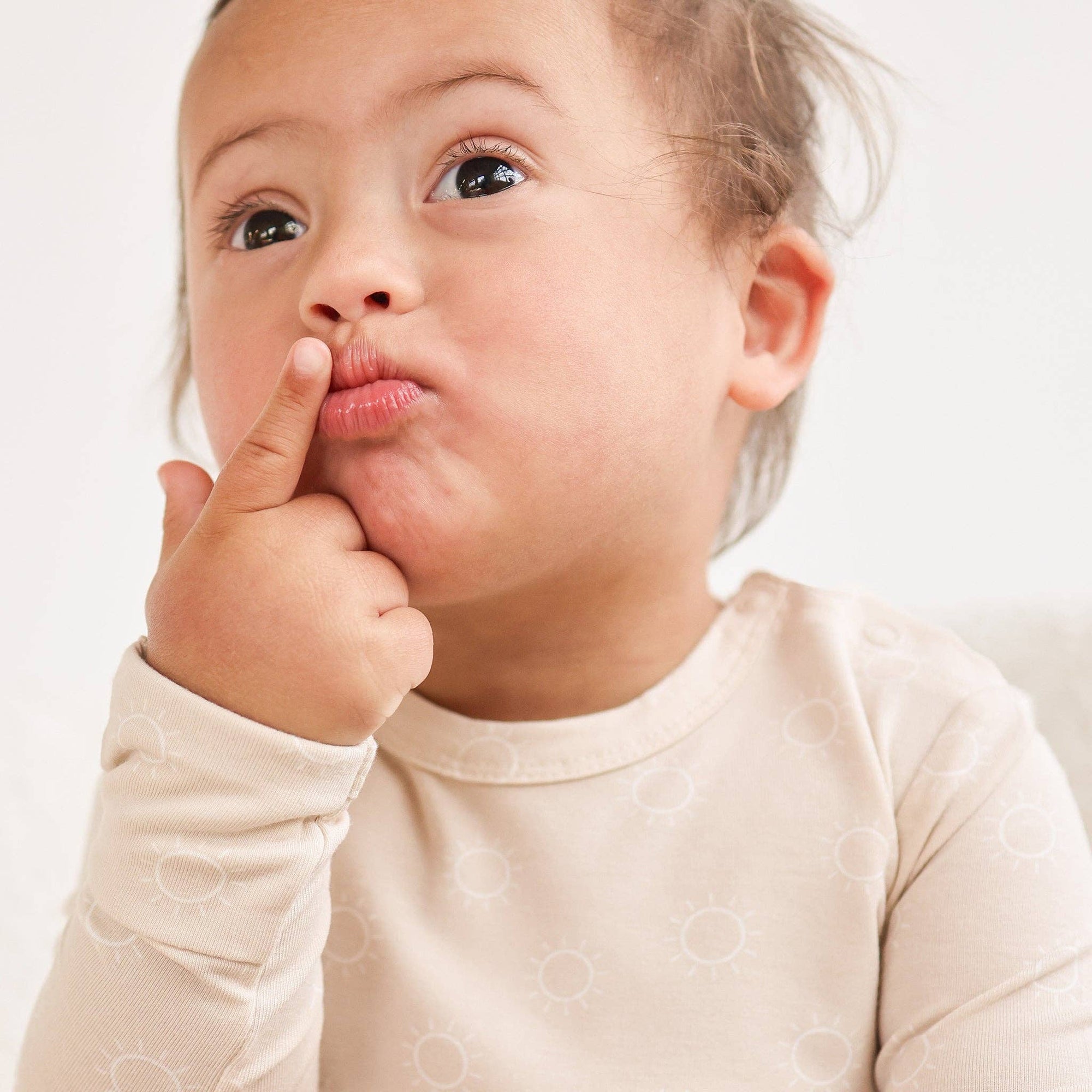 Child wearing a beige long-sleeve shirt with a plain background