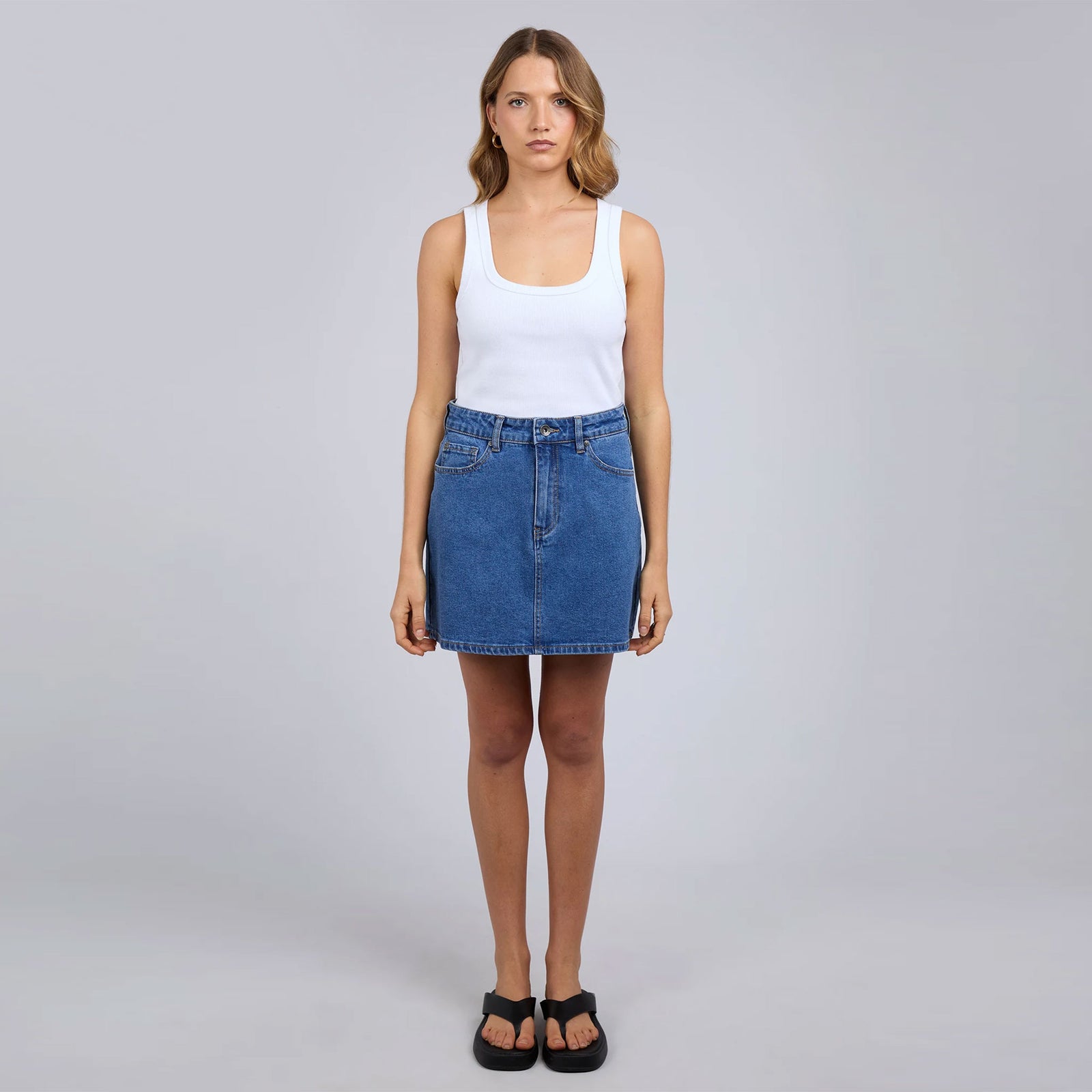 Woman wearing a white tank top and blue denim skirt on a gray background