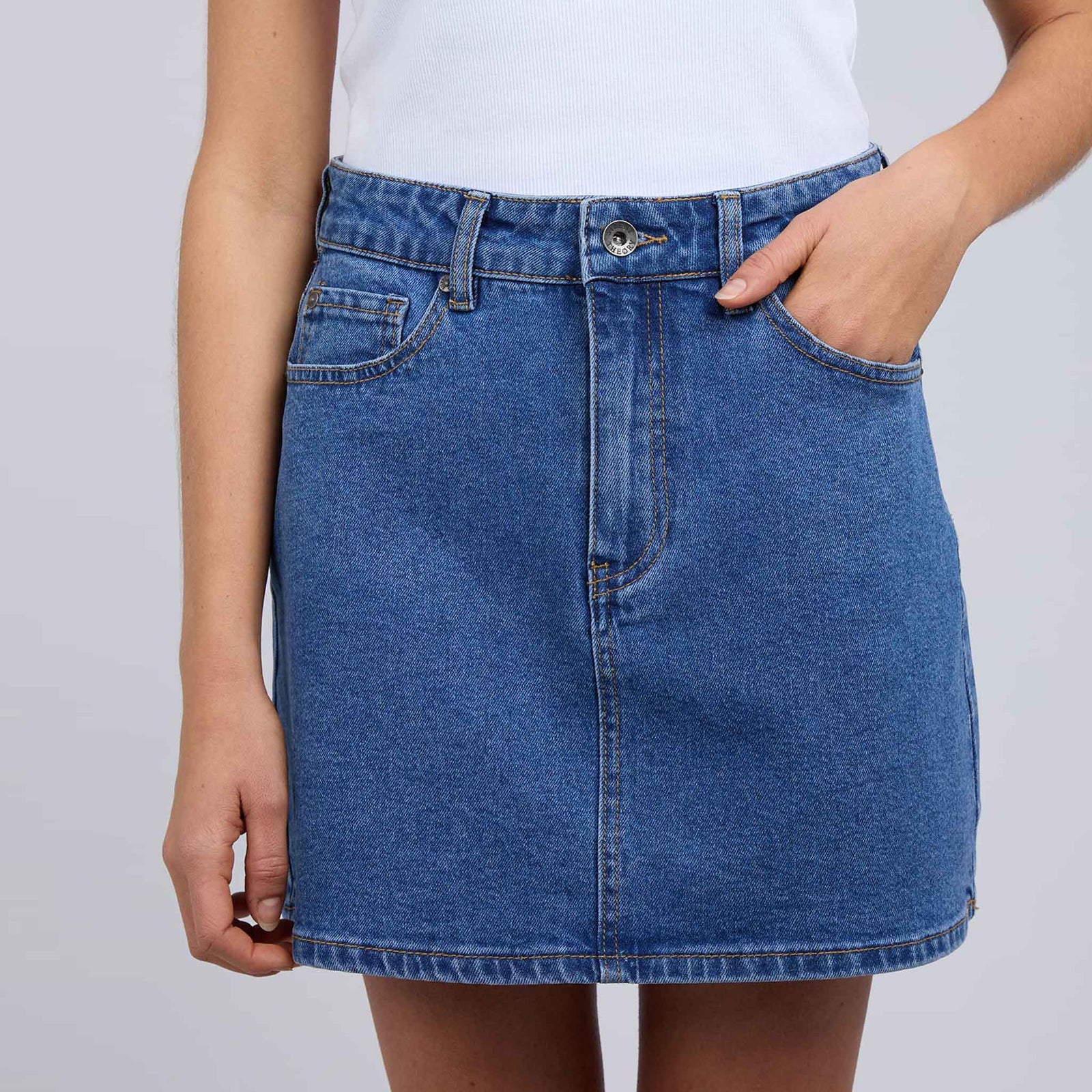 Woman wearing a white tank top and blue denim skirt on a gray background