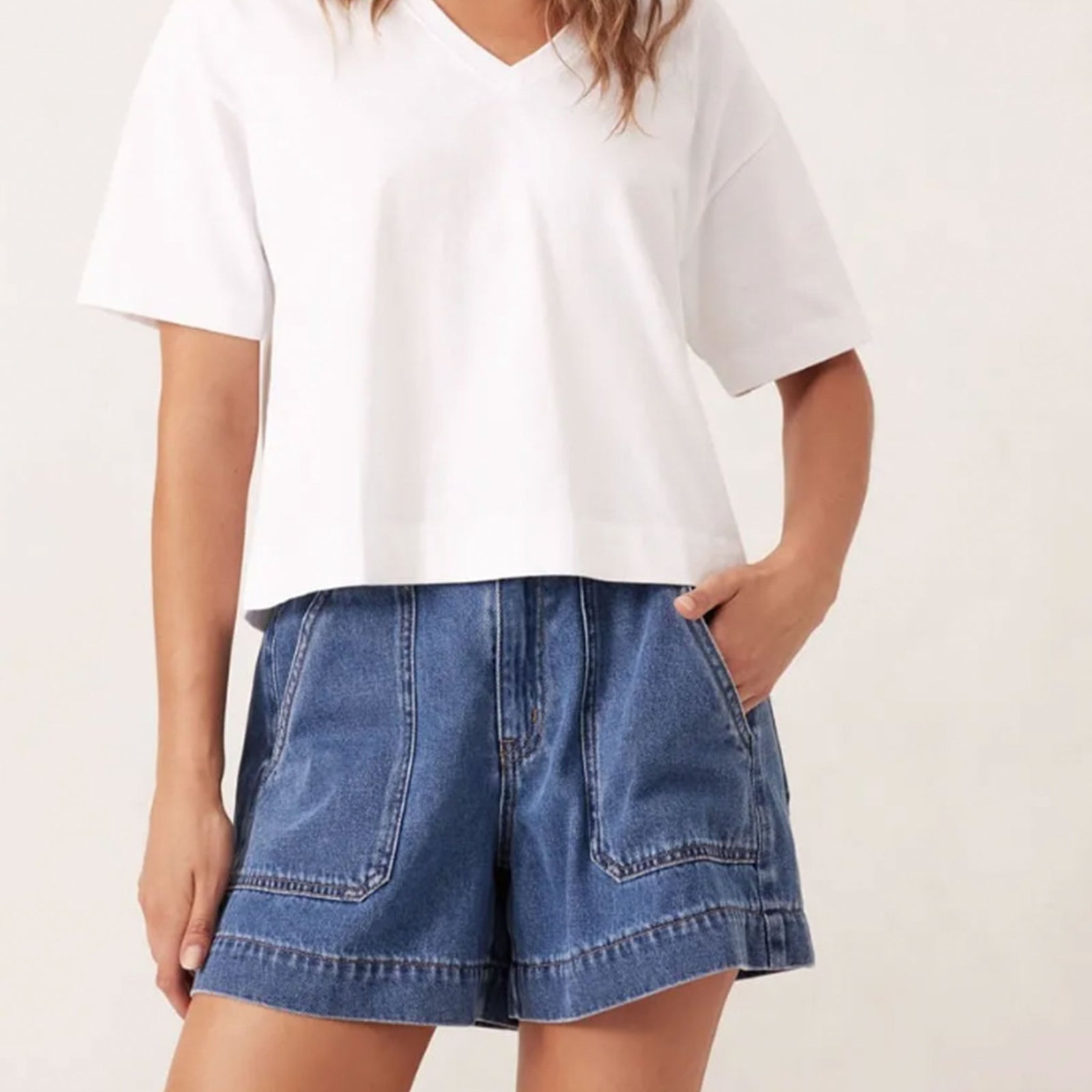 Person wearing a white t-shirt and blue denim shorts on a plain background
