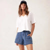 Woman wearing a white t-shirt and blue denim shorts with a plain background