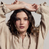 Woman wearing a beige shirt with arms raised against a plain background
