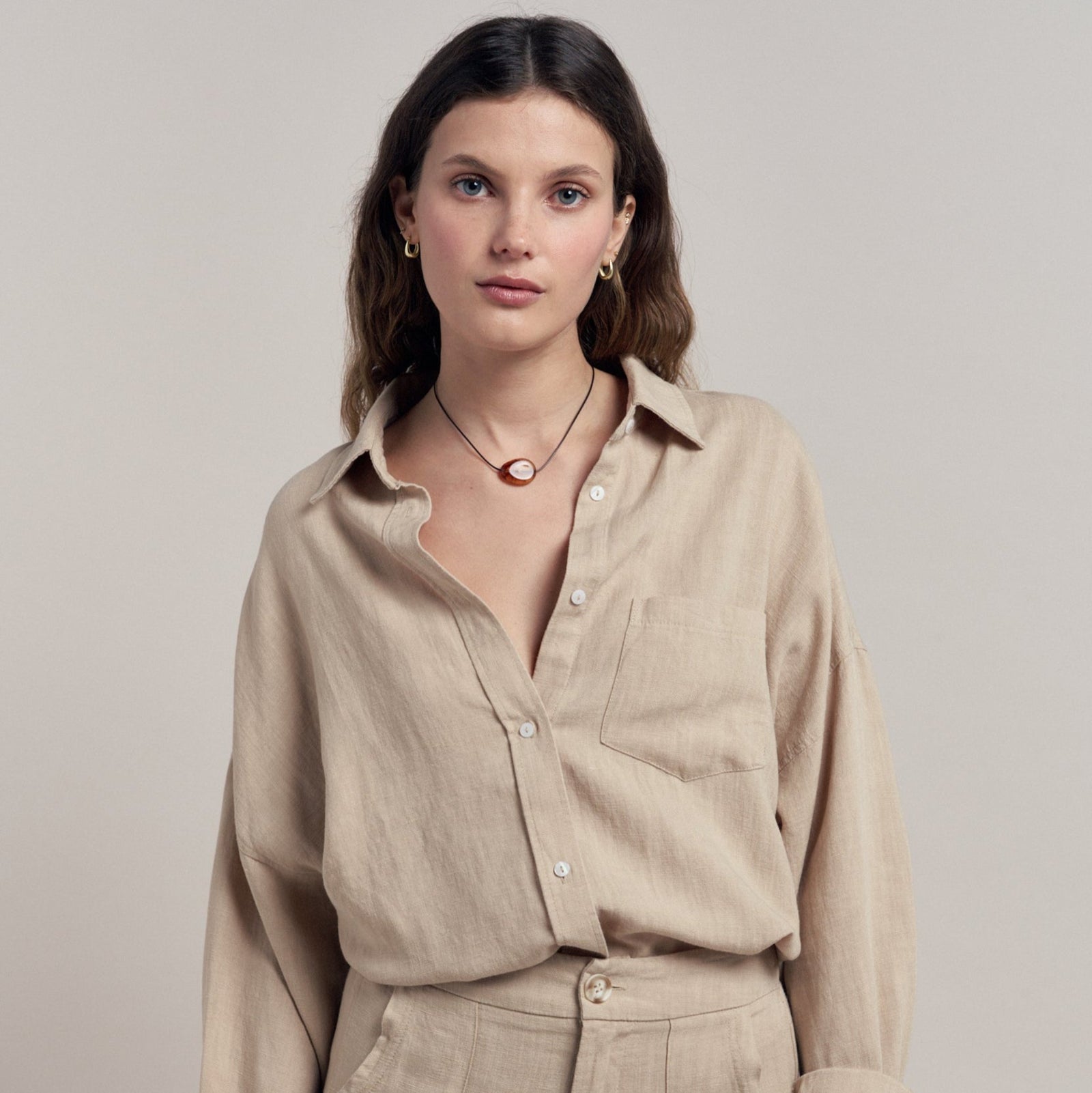 Woman wearing a beige shirt and pants against a plain background