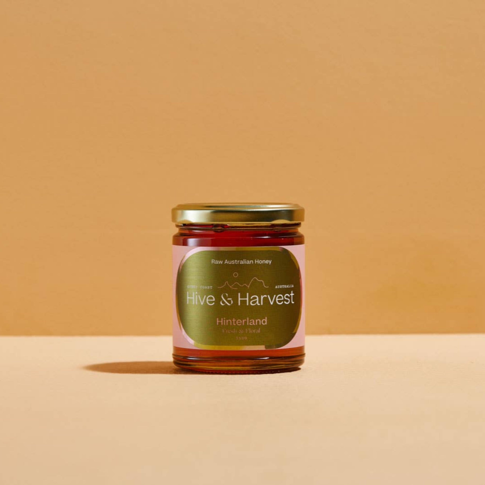 Jar of honey labeled 'Hive & Harvest' on a beige background