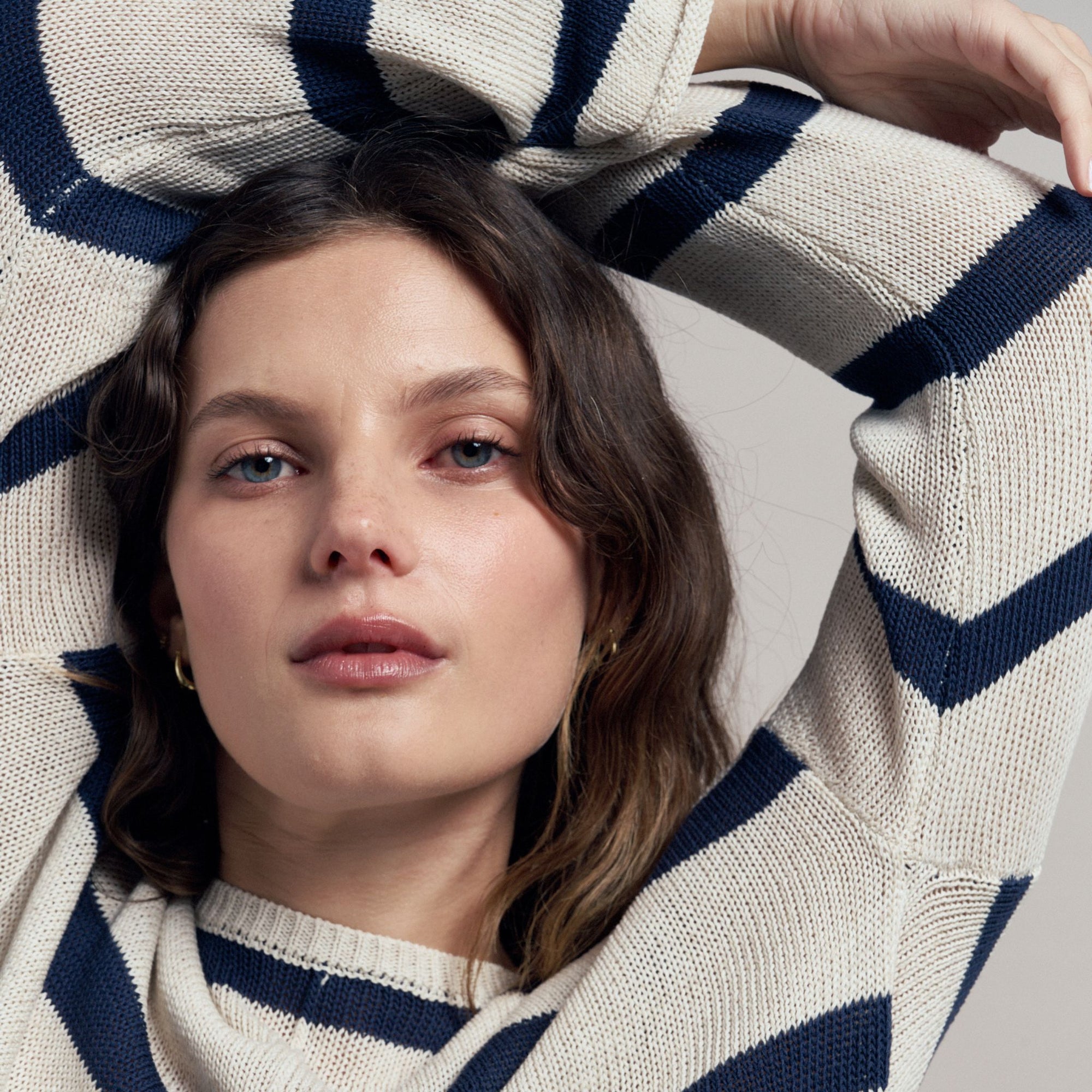Woman wearing a white sweater with navy blue stripes against a plain background