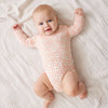 Baby wearing a pink floral onesie lying on a white textured blanket