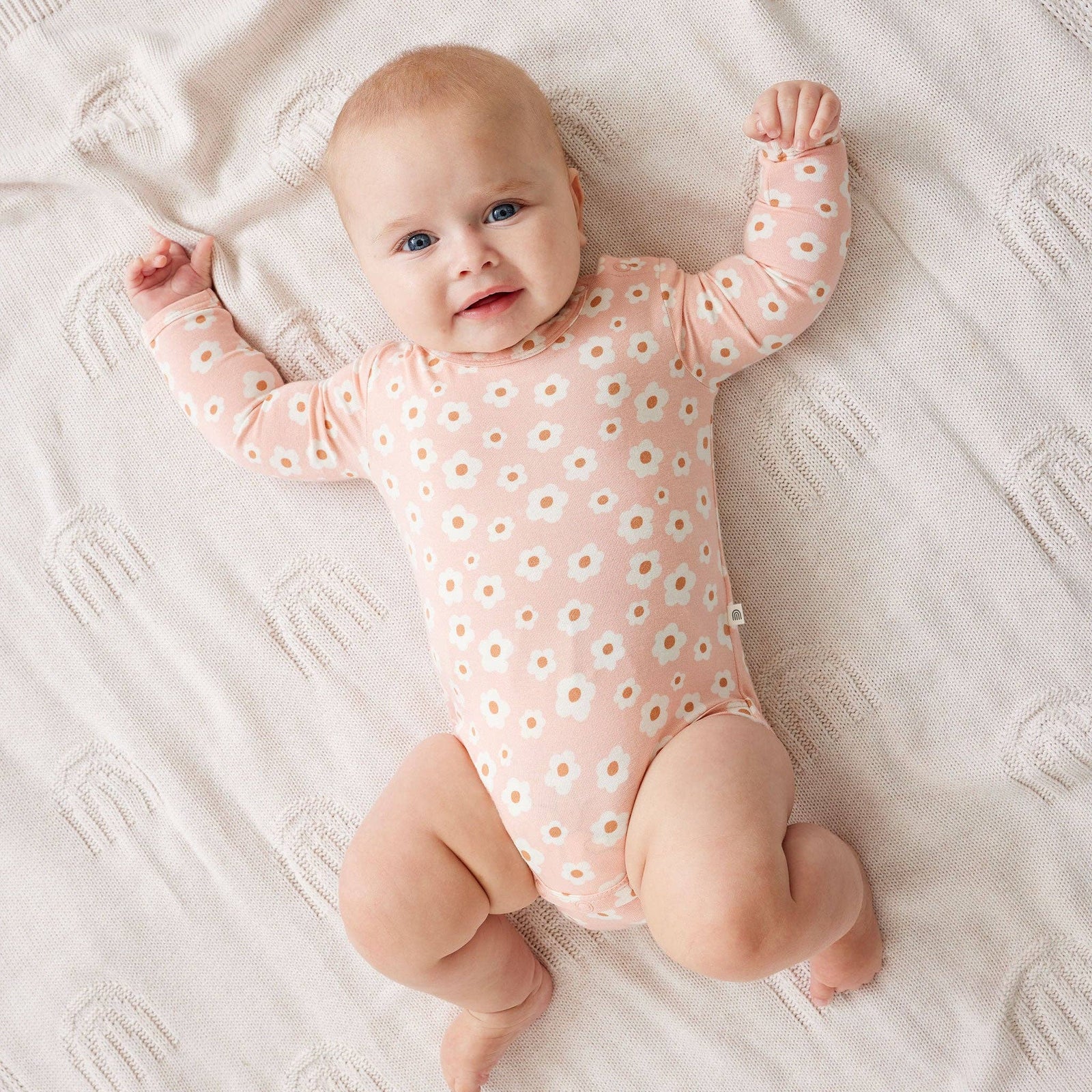 Baby wearing a pink onesie with white floral patterns on a white blanket.