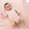 Baby in a pink floral outfit lying on a pink floral blanket