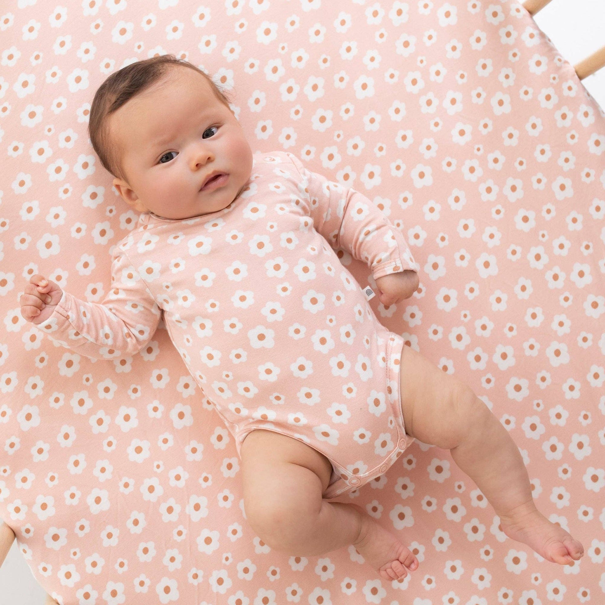 Baby in a pink floral outfit lying on a pink floral blanket
