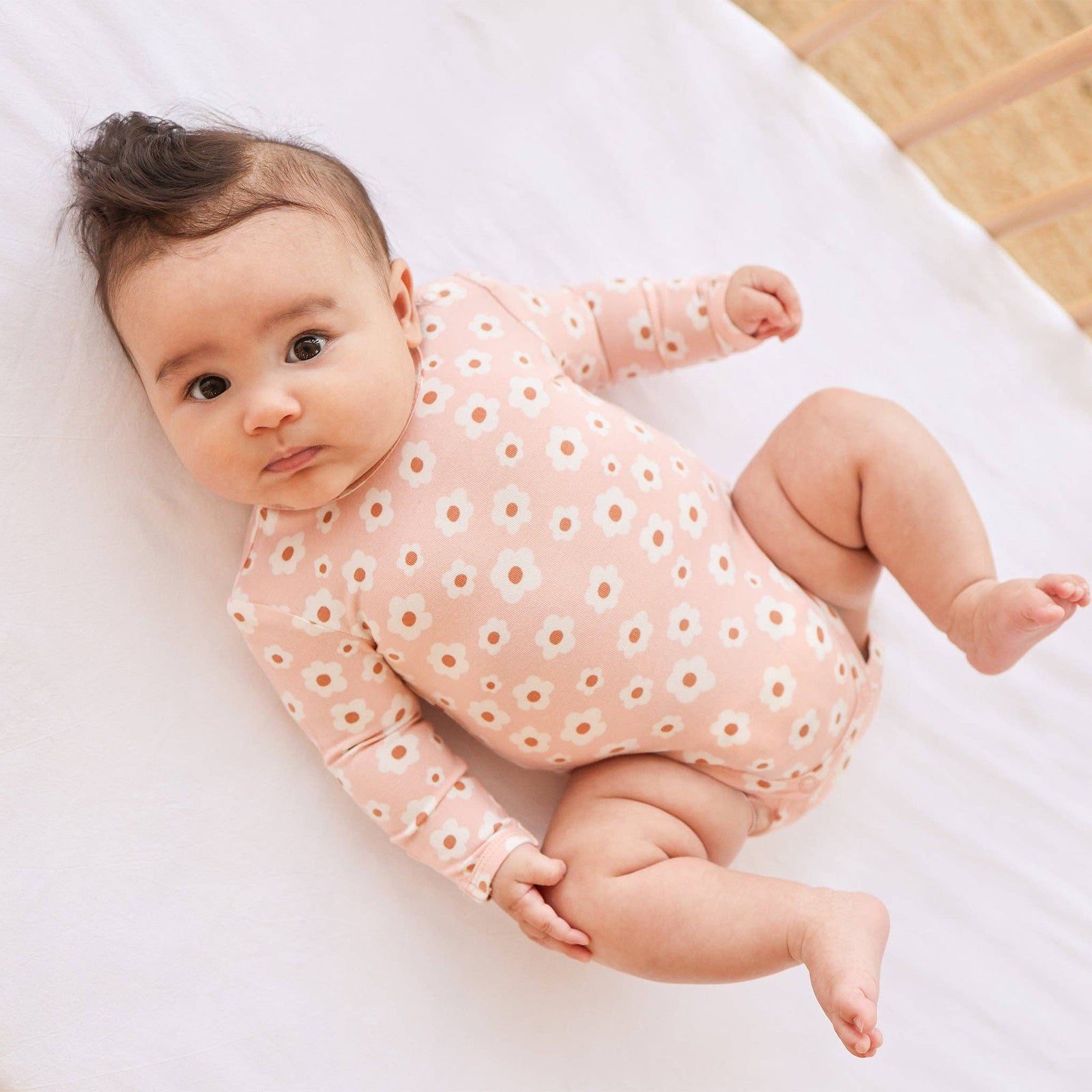 Baby wearing a pink onesie with white floral patterns on a white blanket.