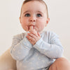 Baby wearing a light blue onesie with white patterns, sitting on a beige surface.