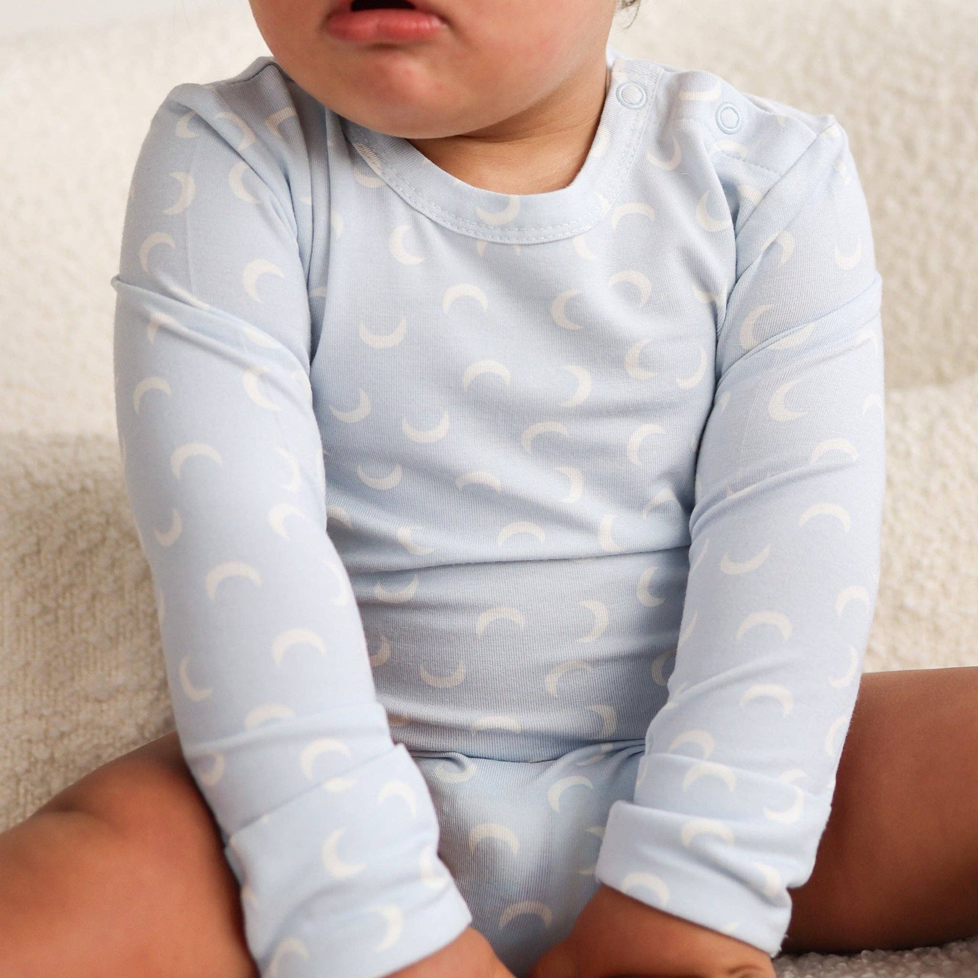 Baby wearing a light blue onesie with crescent moon patterns on a neutral background