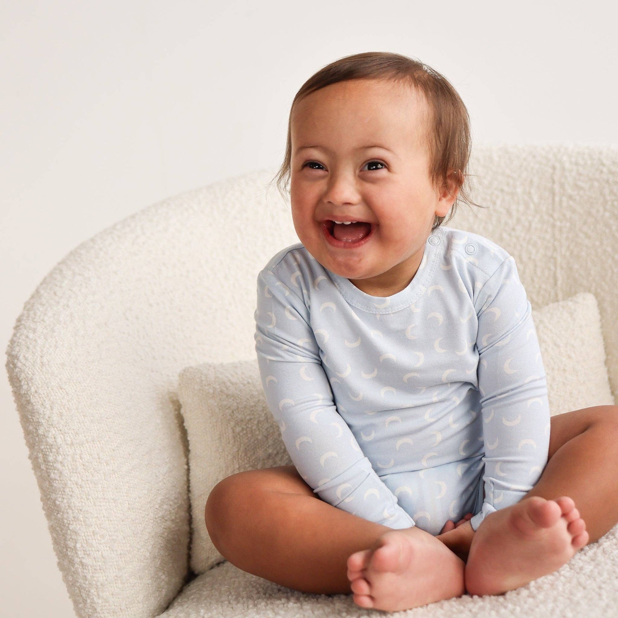 Child wearing a light blue onesie with white patterns, sitting on a white couch.