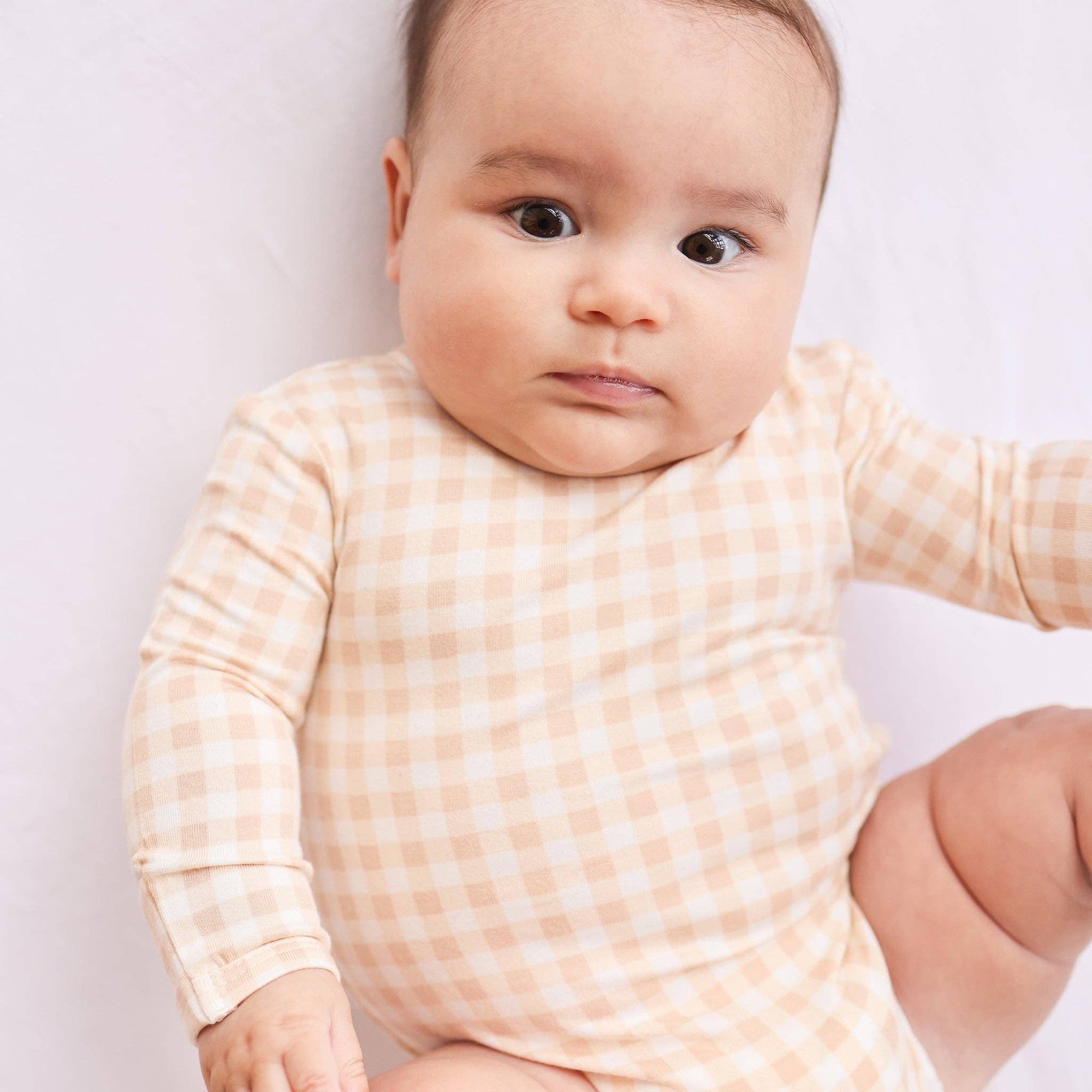 Baby wearing a peach checkered onesie against a light background