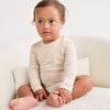 Baby wearing a beige long-sleeve onesie sitting on a white couch.