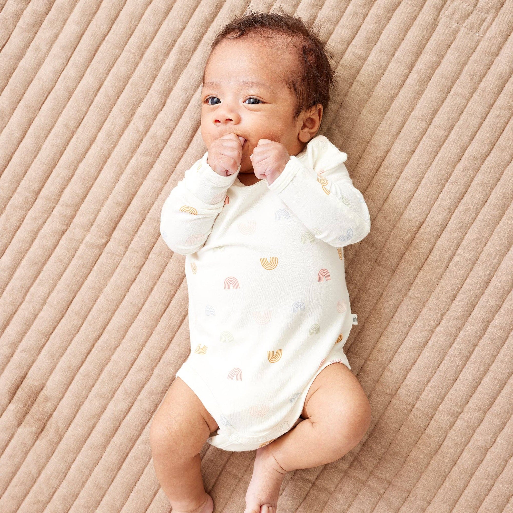Baby wearing a white onesie with colorful patterns on a beige textured surface