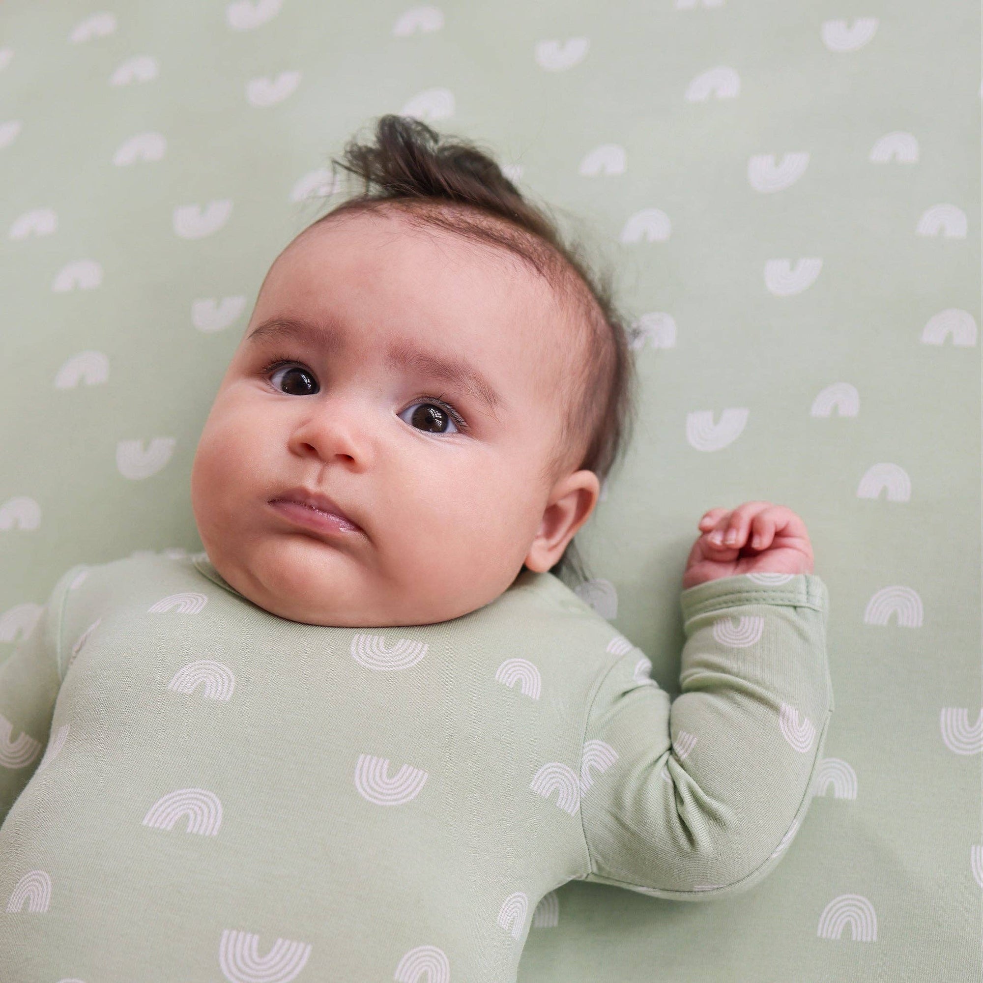 Baby lying on a green crib sheet with heart patterns