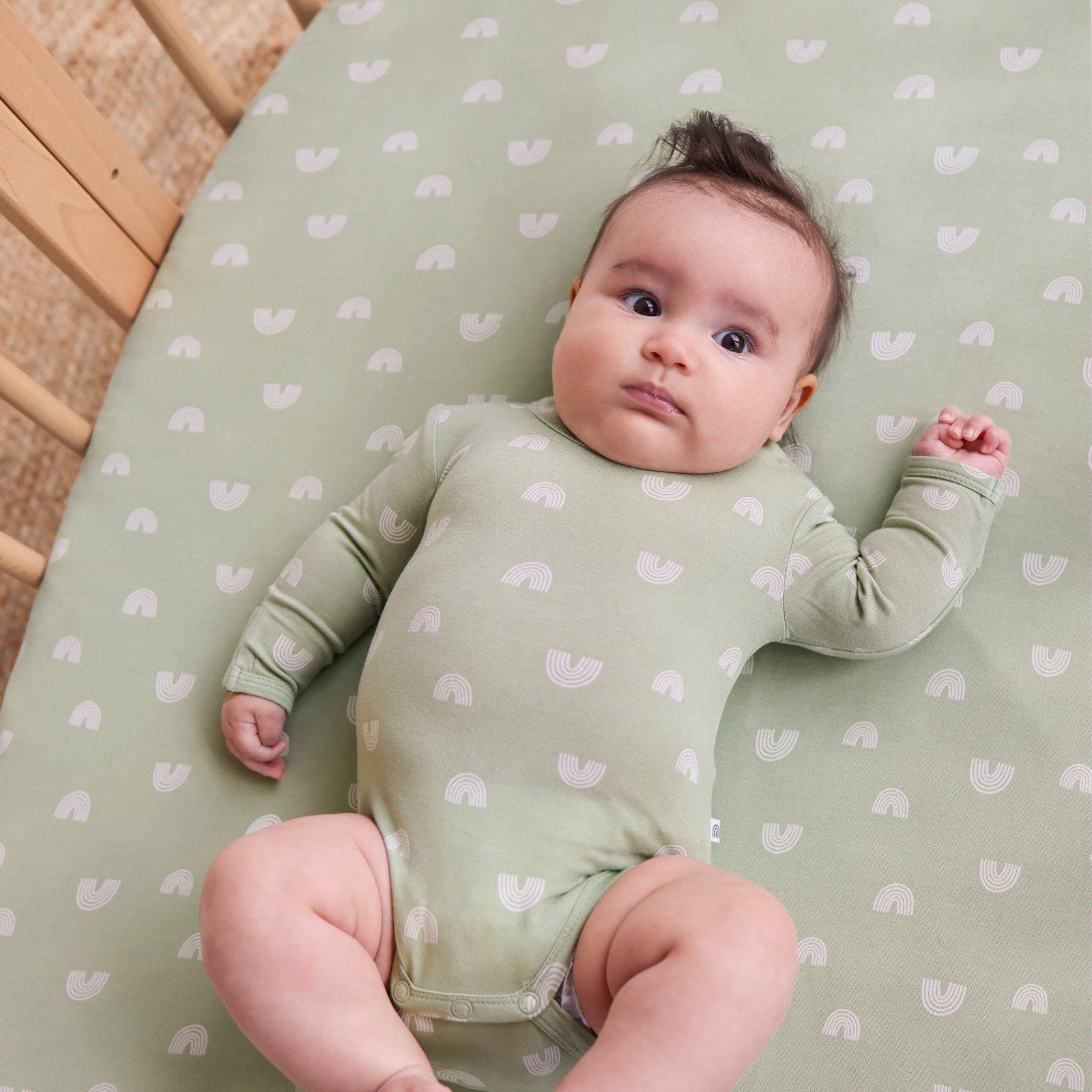 Baby lying on a green crib sheet with heart patterns