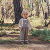 Child in a forest wearing a patterned cardigan and overalls.