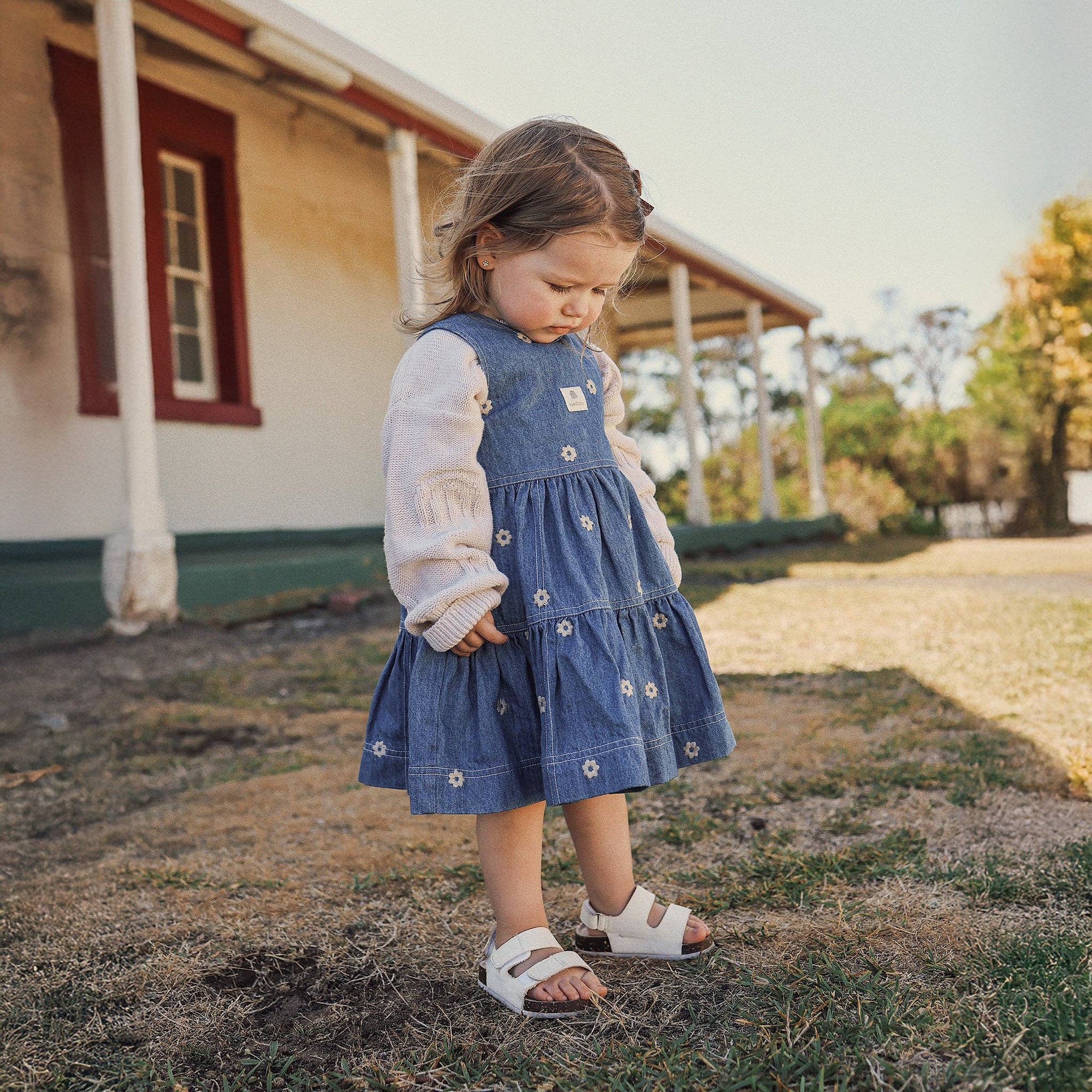 Young girl in a blue dress standing in front of a house