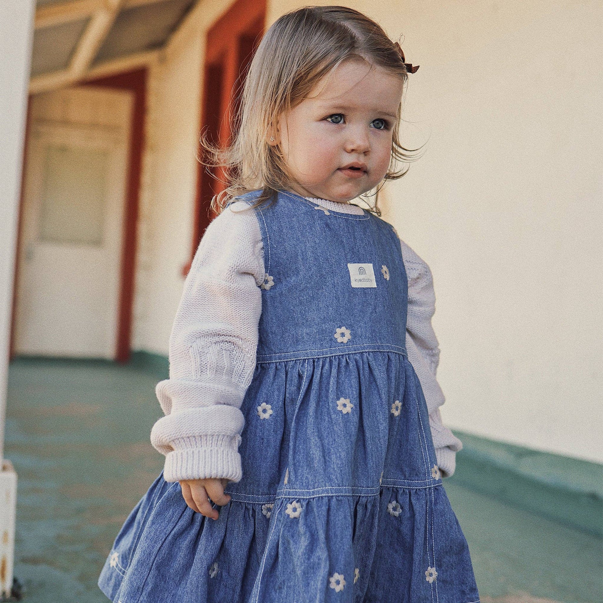 Young girl wearing a blue dress with white flowers outdoors.