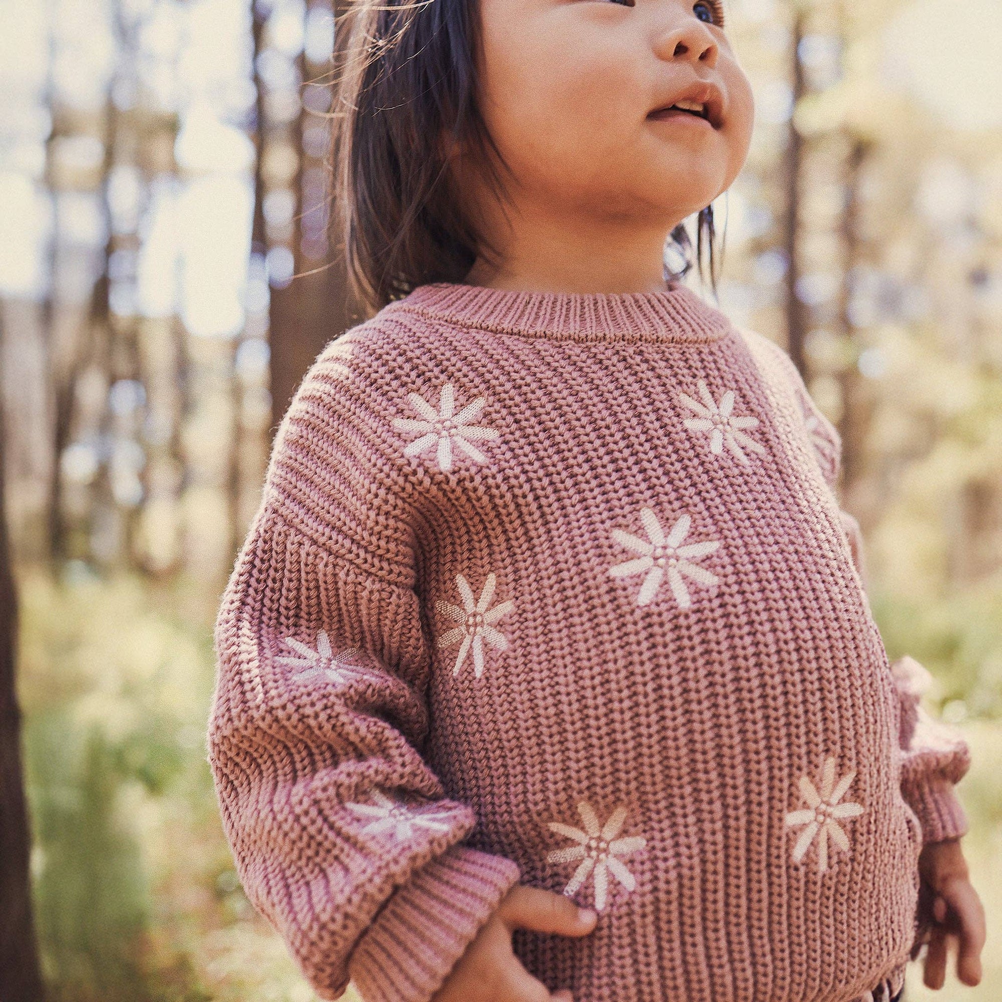 Child wearing a pink sweater and pants with snowflake patterns in a forest setting