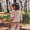 Child in a pink knitted outfit standing in a forest