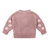Pink knitted cardigan with white floral patterns on sleeves against a white background