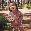 Child wearing a pink sweater and pants with snowflake patterns in a forest setting