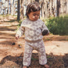 Child in a floral outfit holding a pine cone in a forest setting