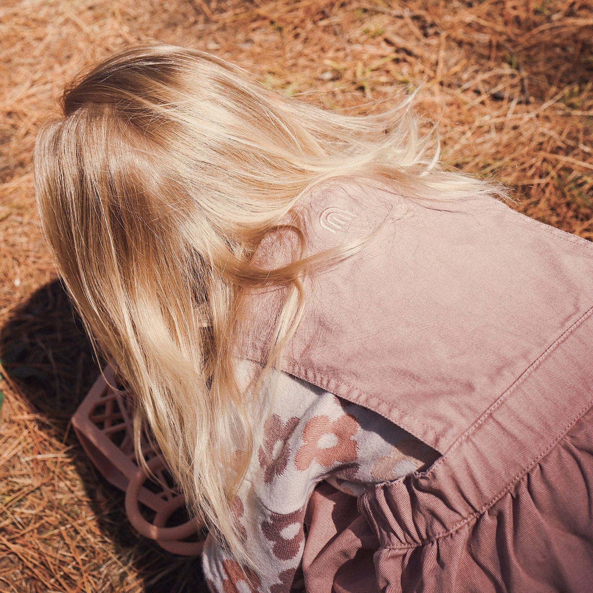 Person wearing a pink jacket with floral patterned shirt underneath, standing on dry grass.