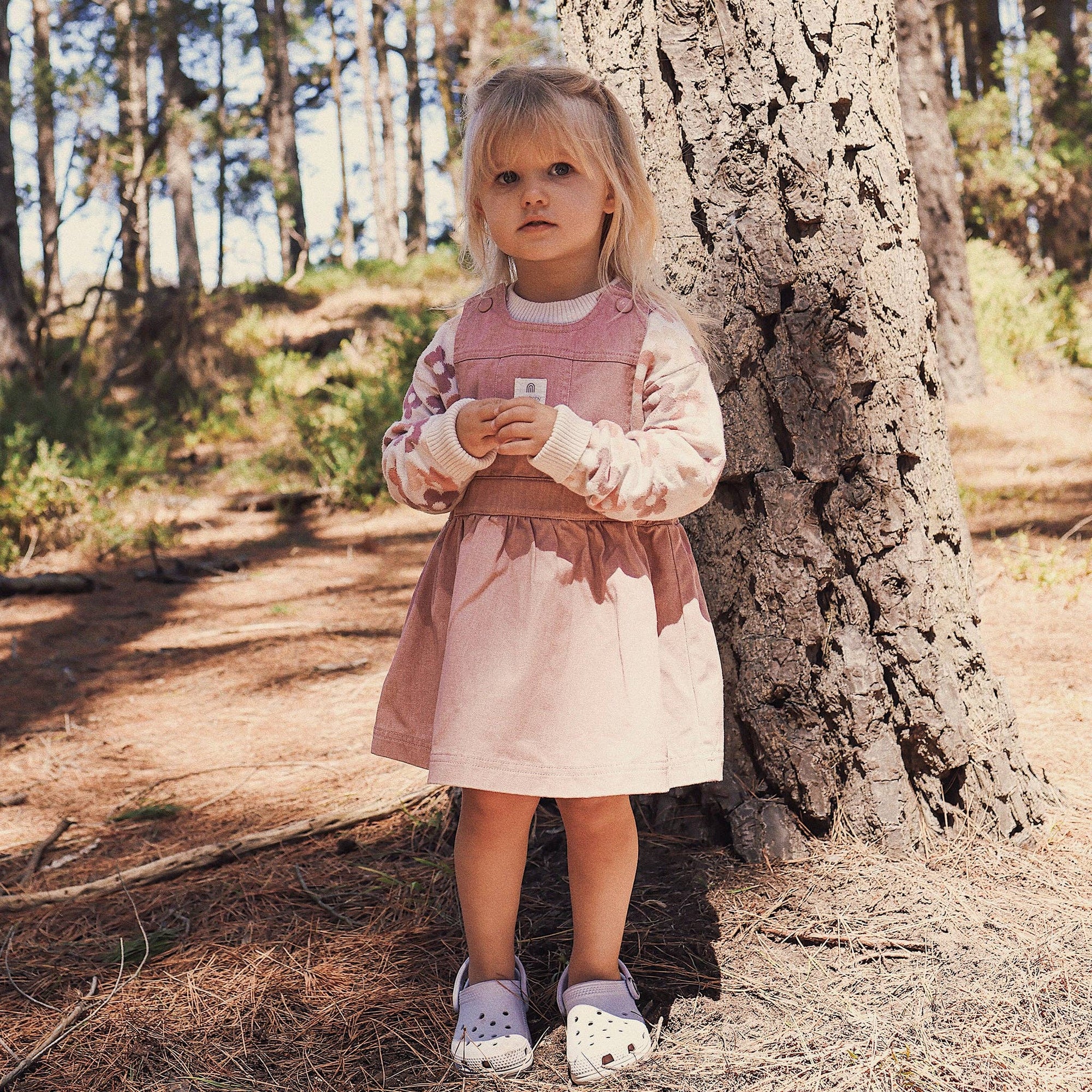 Young girl in a pink dress standing next to a tree in a forest