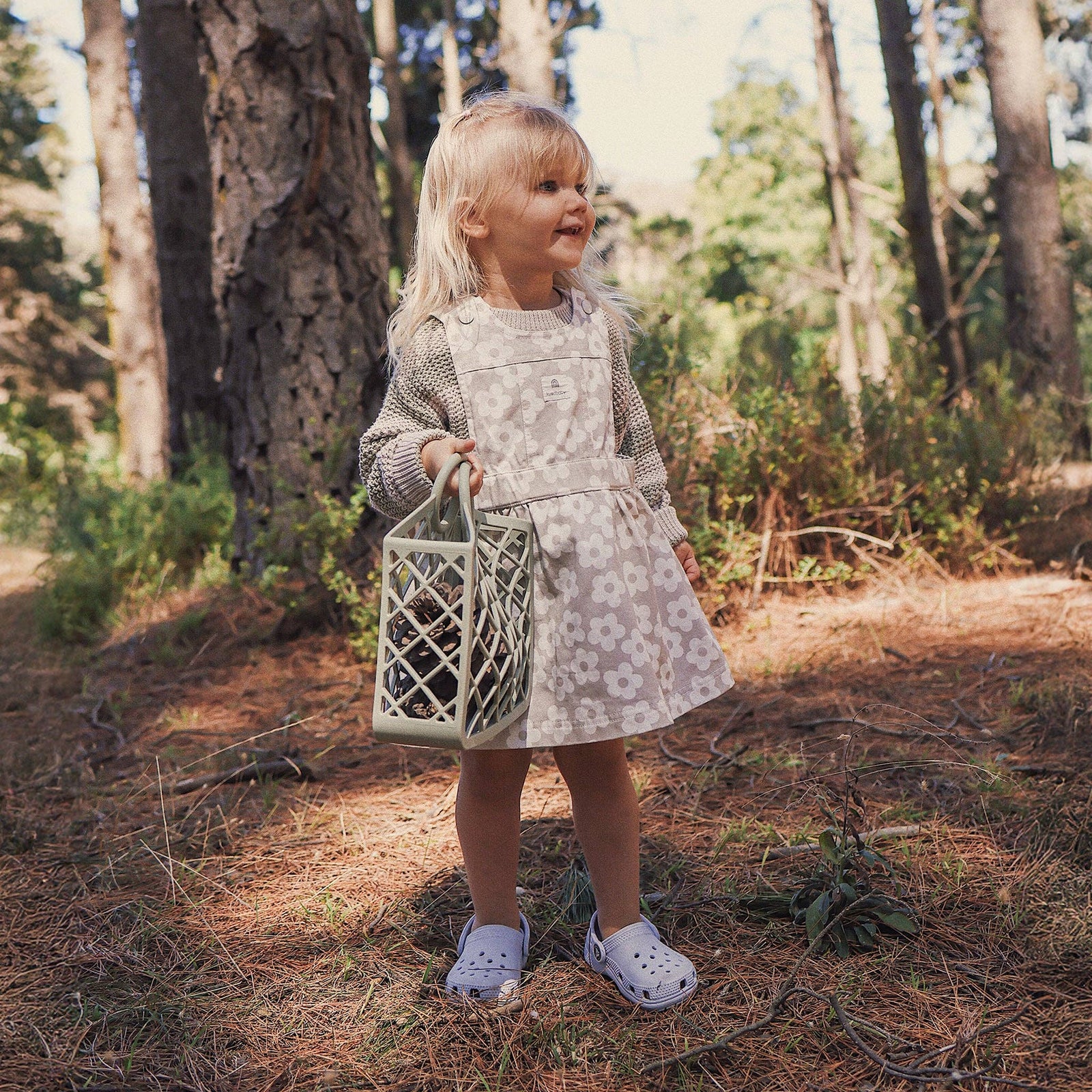 Child wearing a floral dress with a knit sweater, standing outdoors in a natural setting.