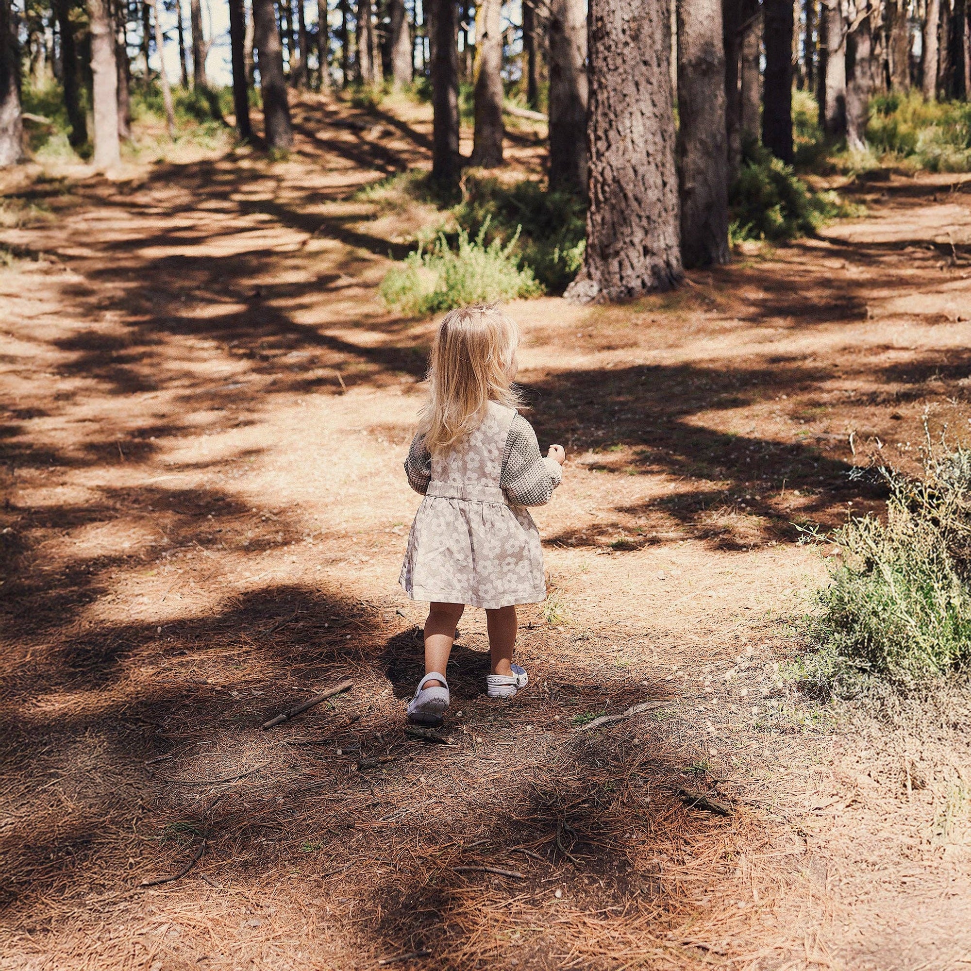 Child in a patterned dress walking on a dirt path through a forest