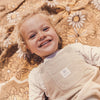 Child wearing a beige outfit with a brand label, lying on a floral-patterned blanket.