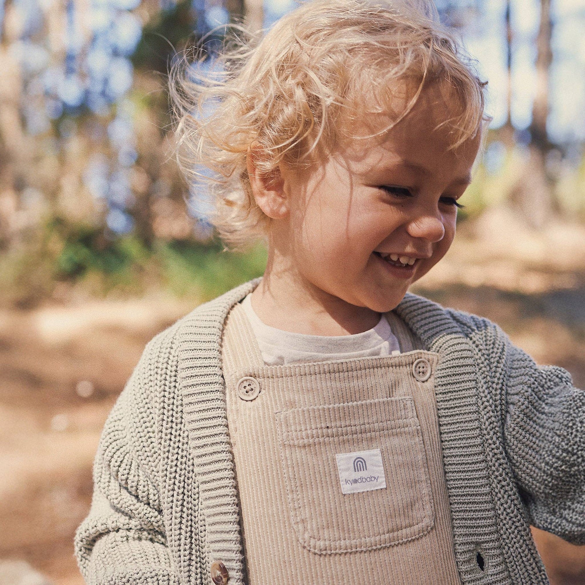 Child wearing a beige corduroy apron with a visible brand label outdoors.