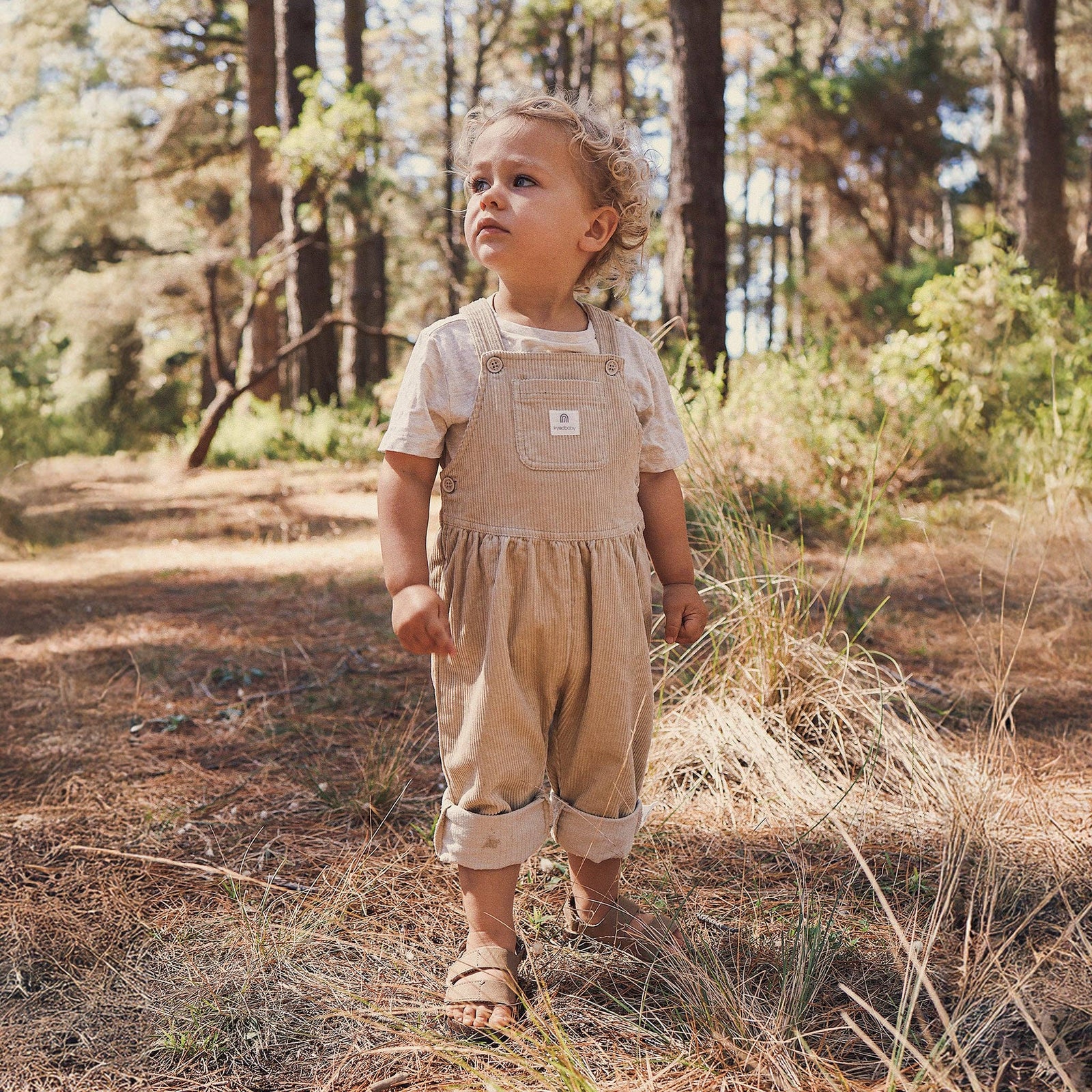 Child in a beige outfit standing in a forest
