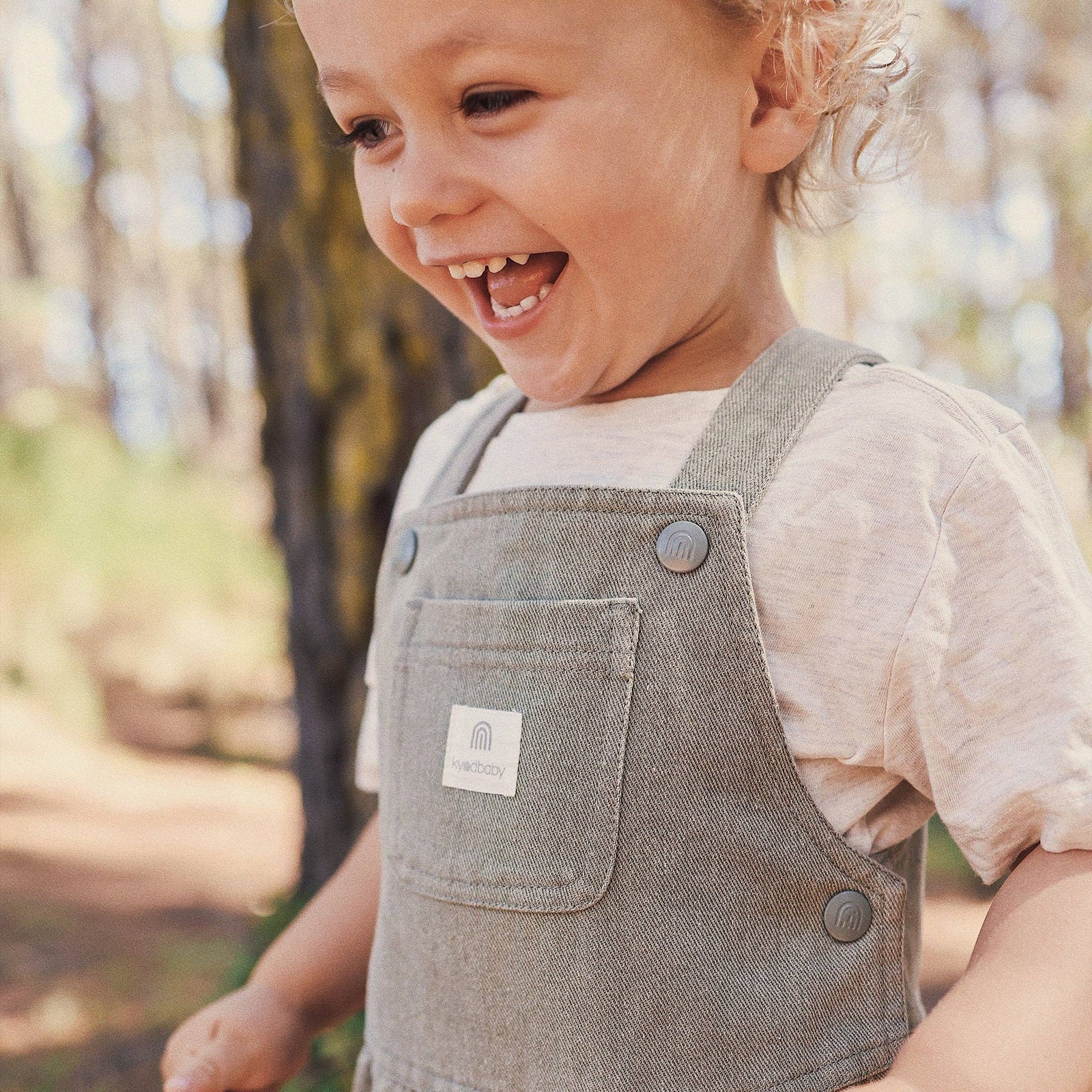 Child in overalls standing in a forest