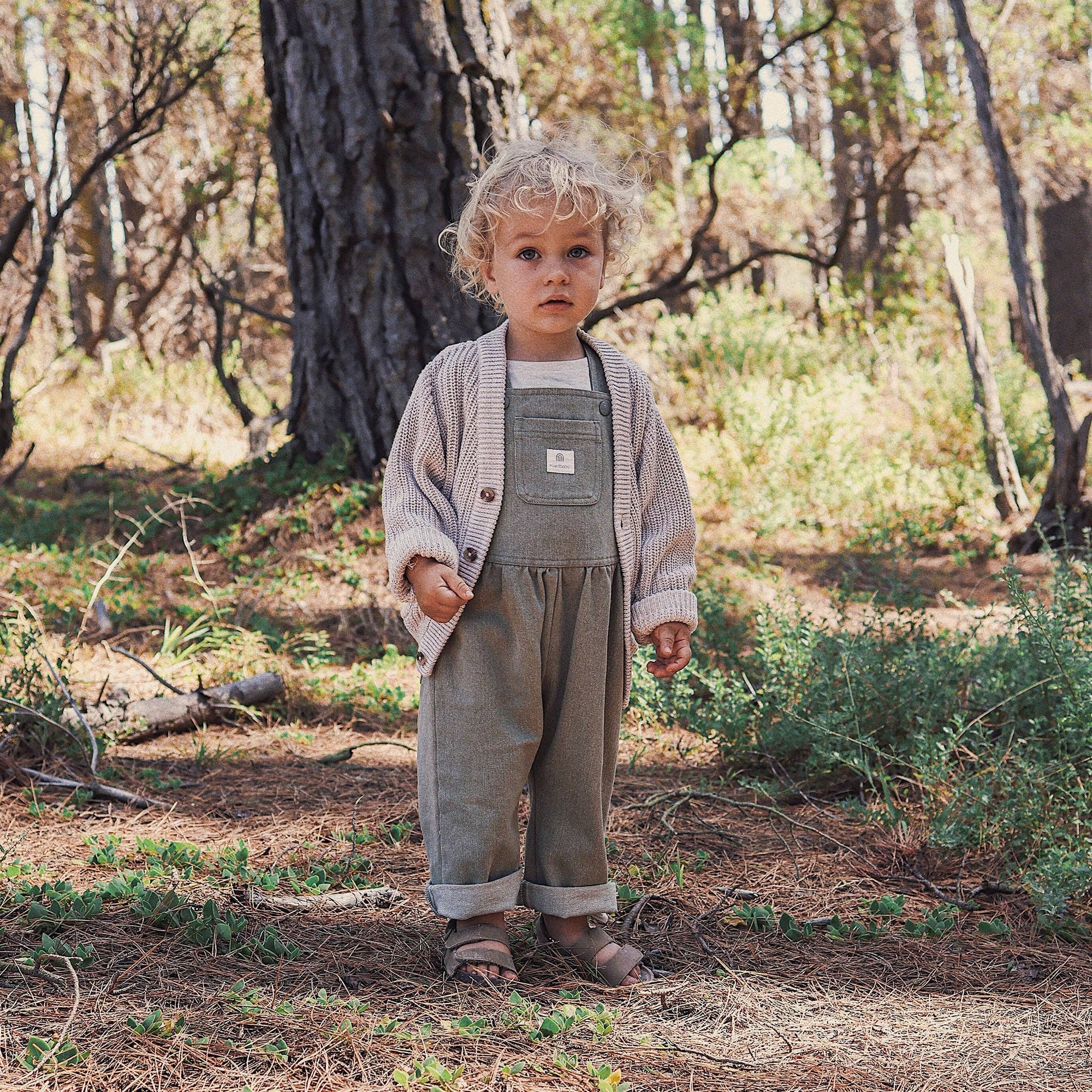 Child in overalls standing in a forest