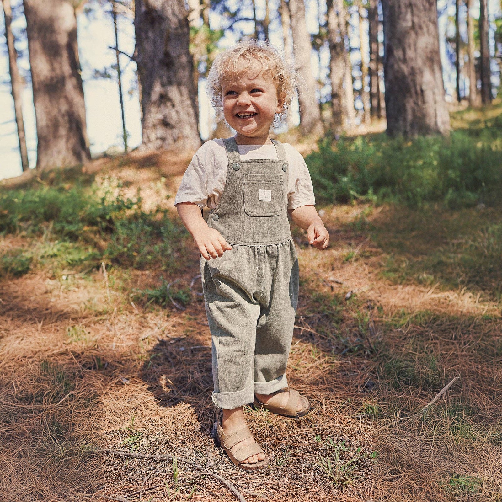 Child in overalls standing in a forest